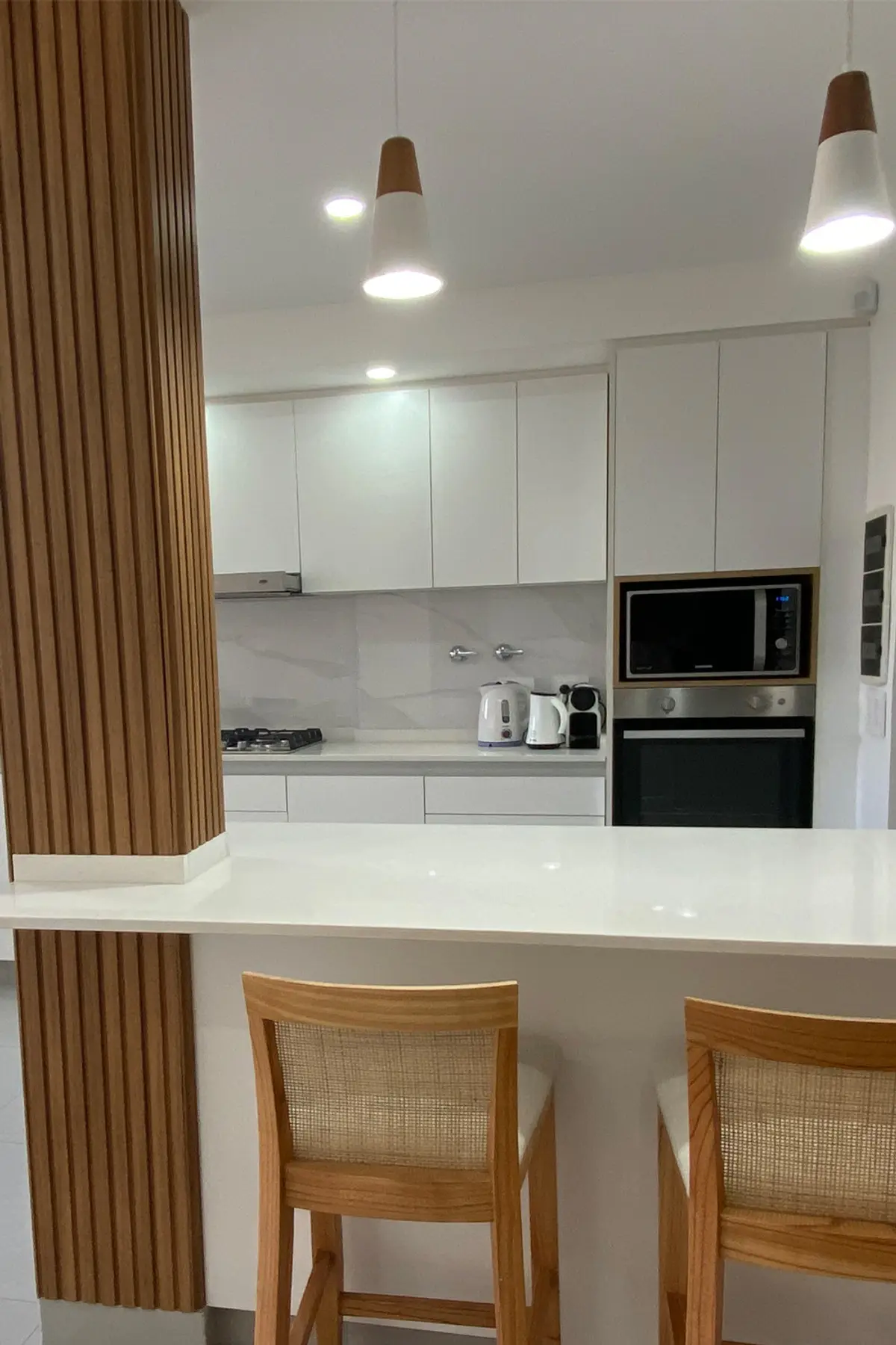 Cocina moderna blanca con isla, detalles en madera y electrodomésticos negros — proyecto COCINA NIEVES, por Estudio Grupo 32, en Buenos Aires