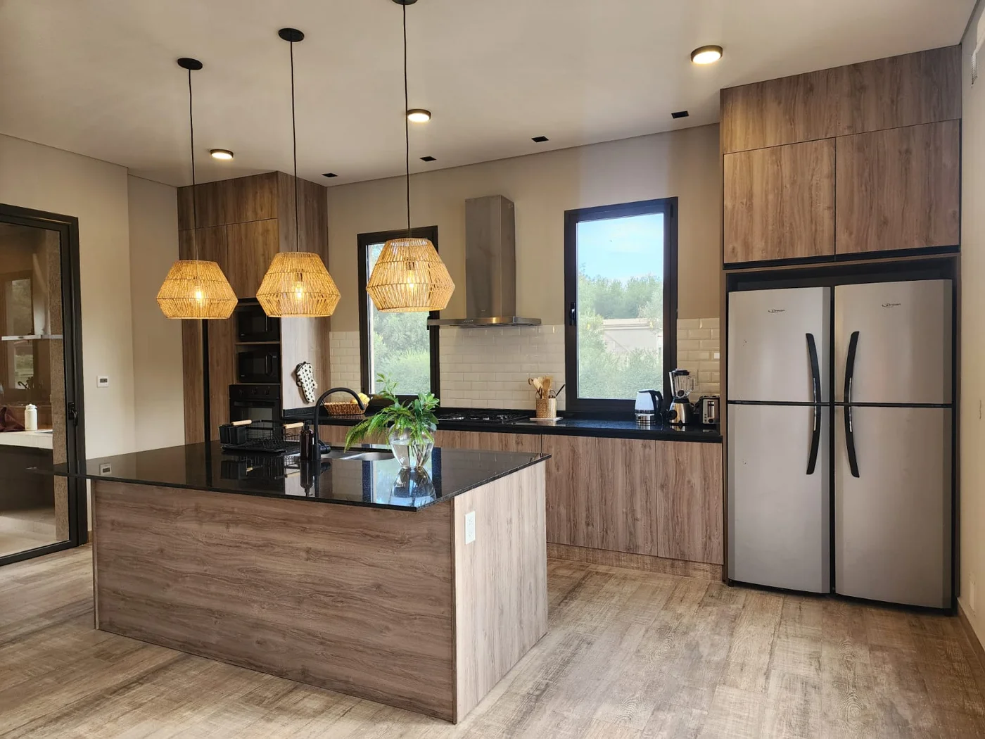 Cocina moderna de madera natural con isla grande y luces colgantes negras.