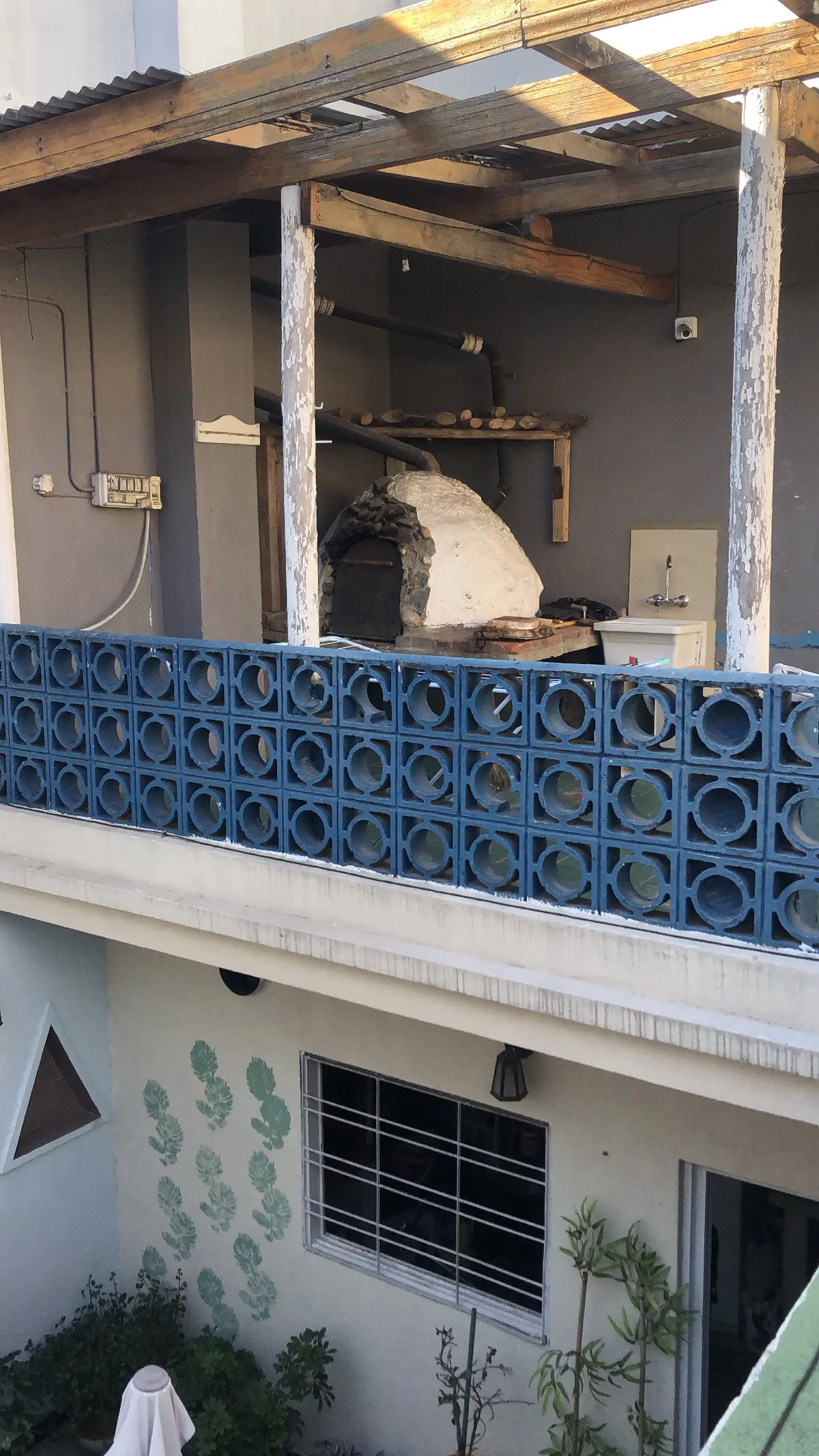Terraço com forno de pedra, pérgola de madeira e grade azul — projeto Marcelo & Majo, por Costantini studio, em Buenos Aires
