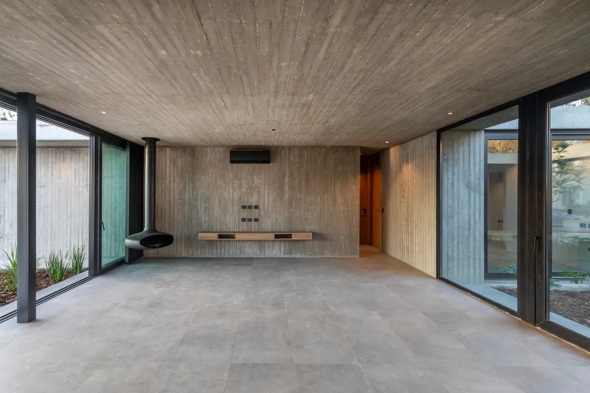 Living moderno minimalista con chimenea colgante y hormigón visto — proyecto Casa ROMA, por V2 Arquitectos, en City Bell