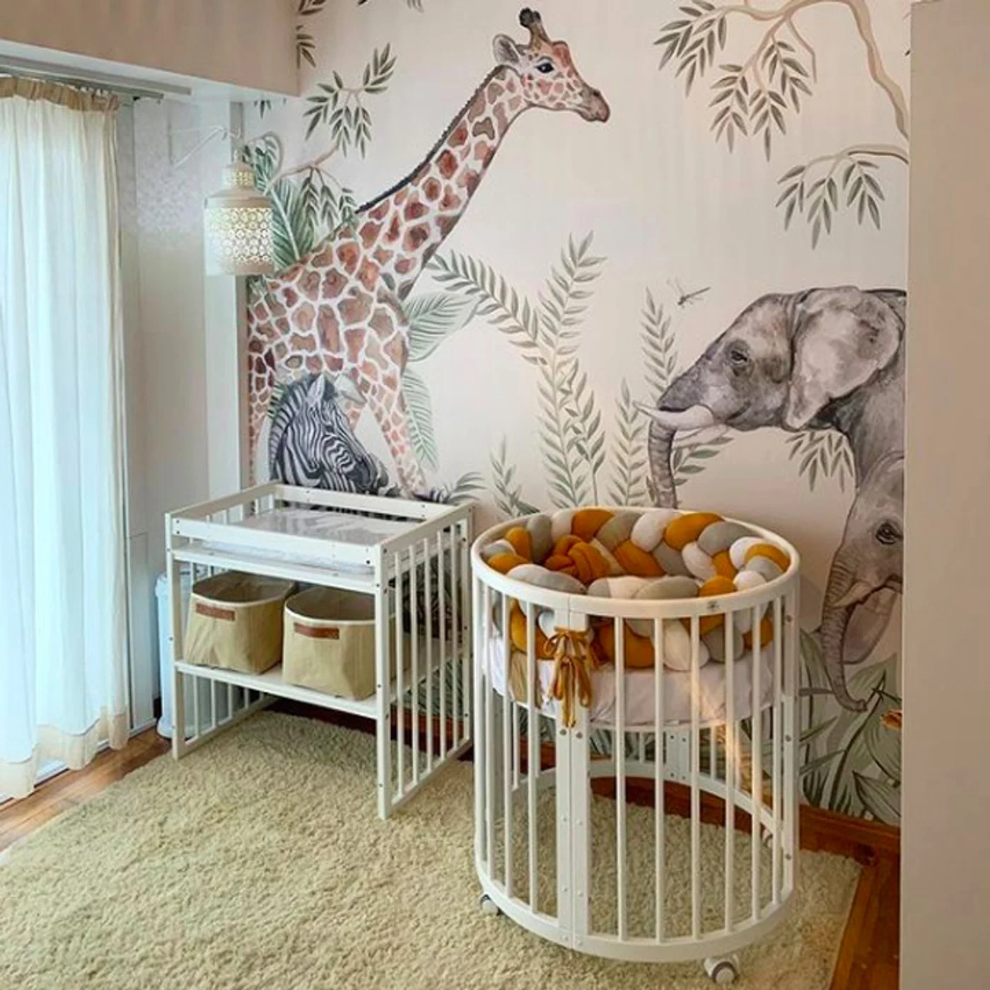 Habitación infantil con mural de animales, cuna redonda y cambiador.