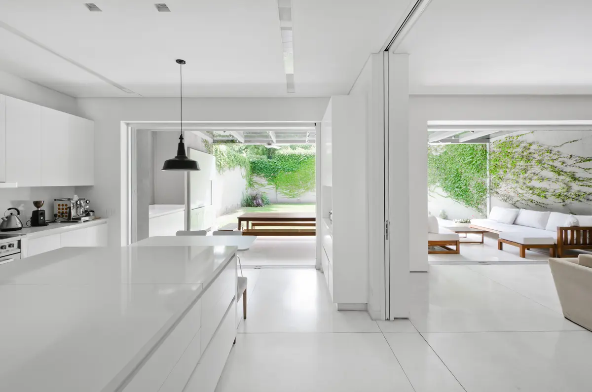 Cozinha e sala minimalista com ilha branca e vegetação externa — projeto Casa D, por Estudio Dado, em Belgrano