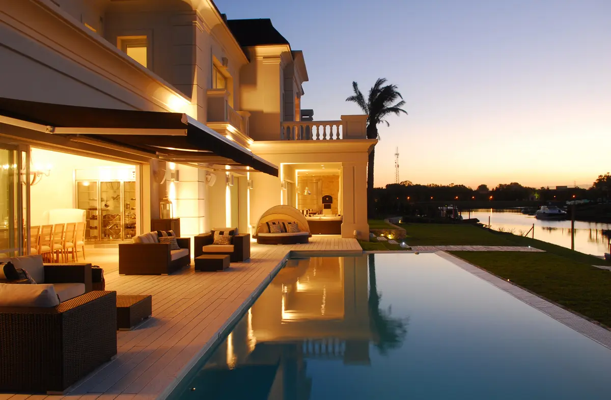 Pileta infinita moderna con mobiliario exterior y luces cálidas al atardecer — proyecto Chateau al Río, por Apaarquitectura, en Tigre