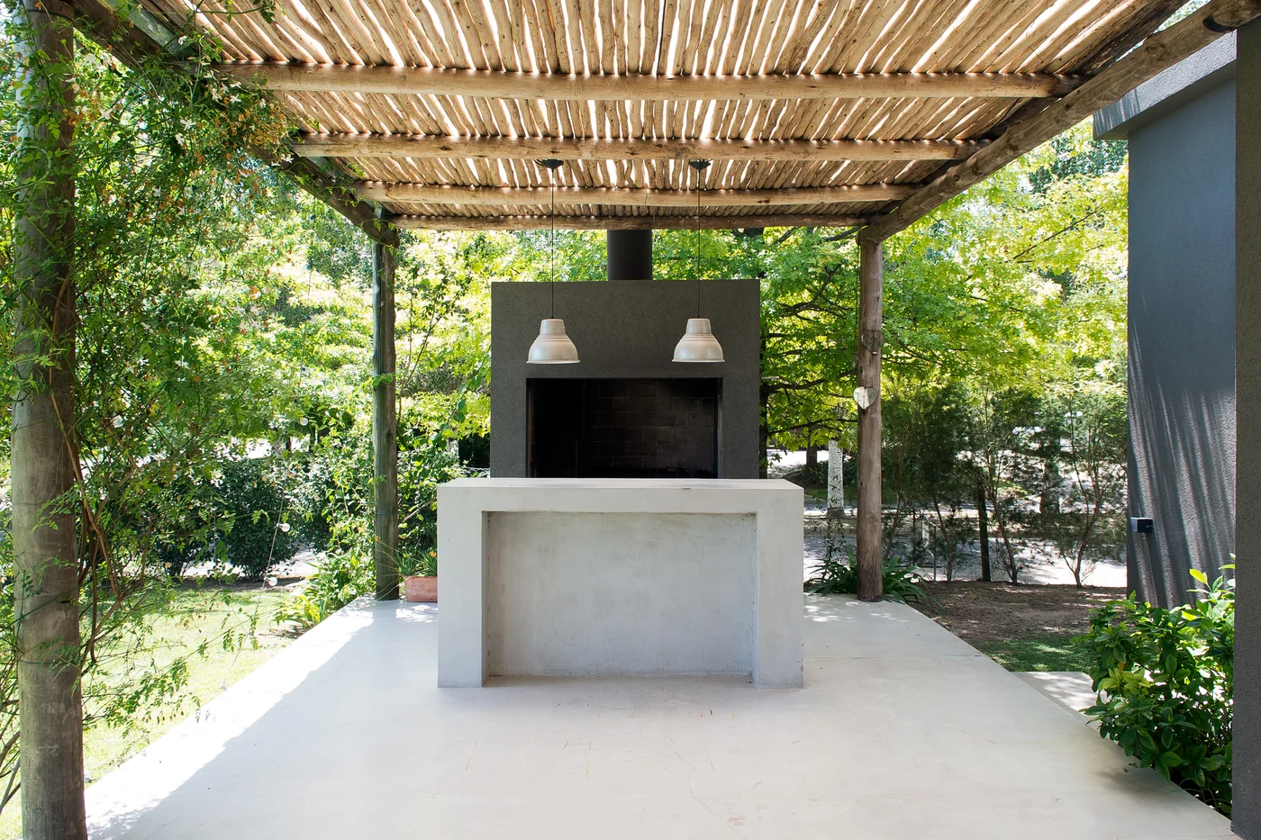 Parrilla exterior moderna con pérgola de madera y mesada de cemento.