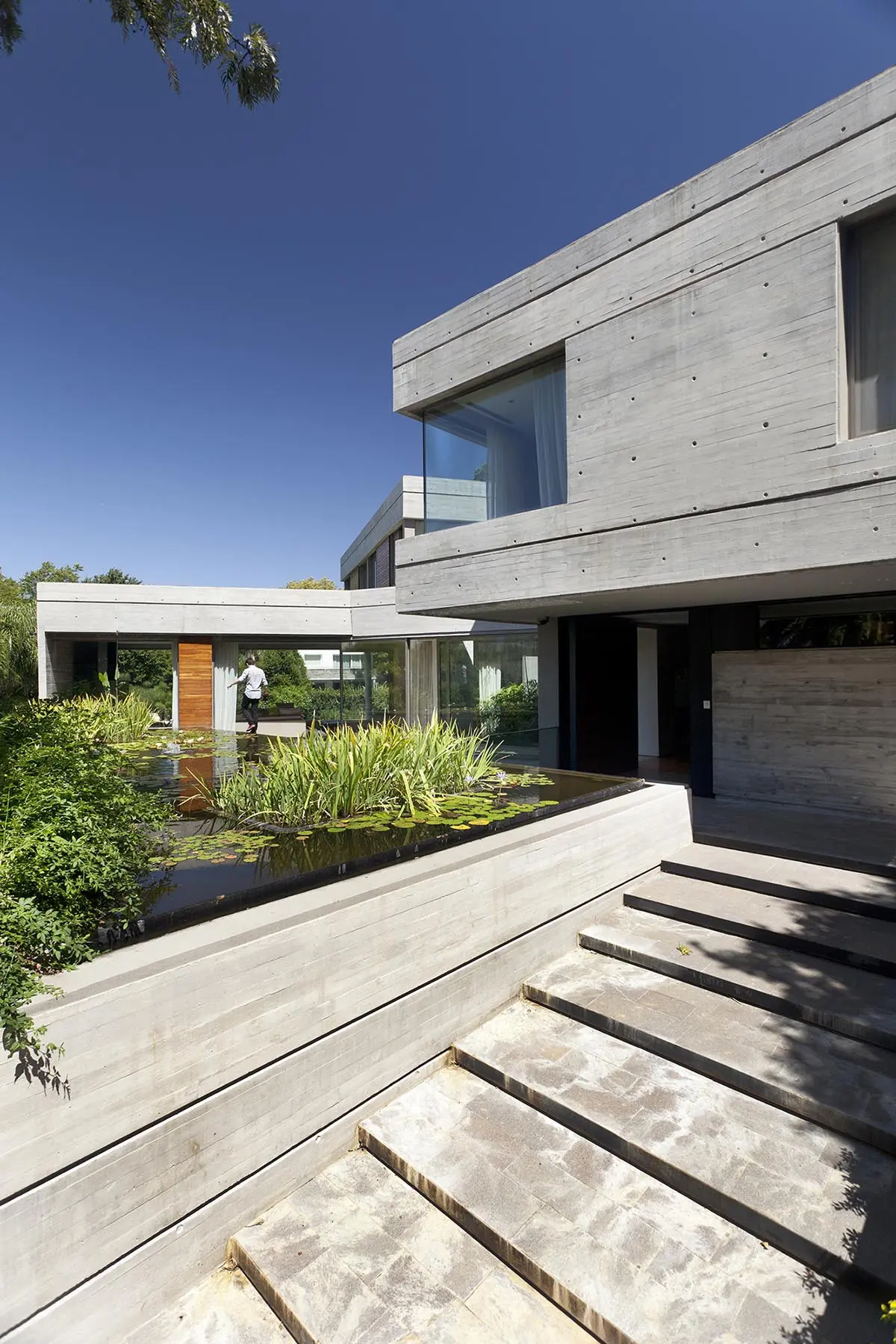 Casa moderna de hormigón visto con estanque y amplias ventanas — proyecto Acasusso, por Remy Arquitectos, en Acassuso