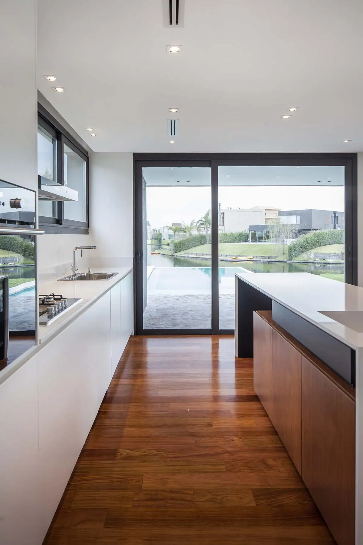Cozinha moderna com ilha e vista para a água, piso de madeira — projeto Alisos, por Remy Arquitectos, em Nordelta