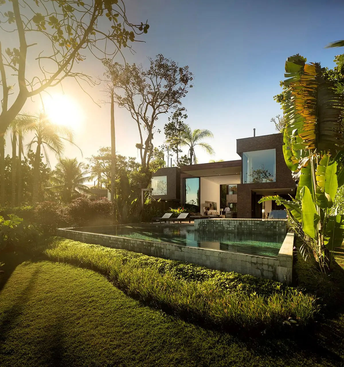 Casa moderna con pileta espejo al atardecer, jardín y vegetación — proyecto West Whales, por Gil Fialho