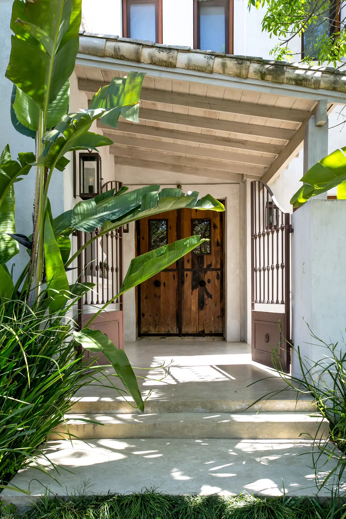 Entrada rústica com portas de madeira e vegetação exuberante — projeto Club Newman 4, por Escalante Vela Arquitectos, em Benavidez