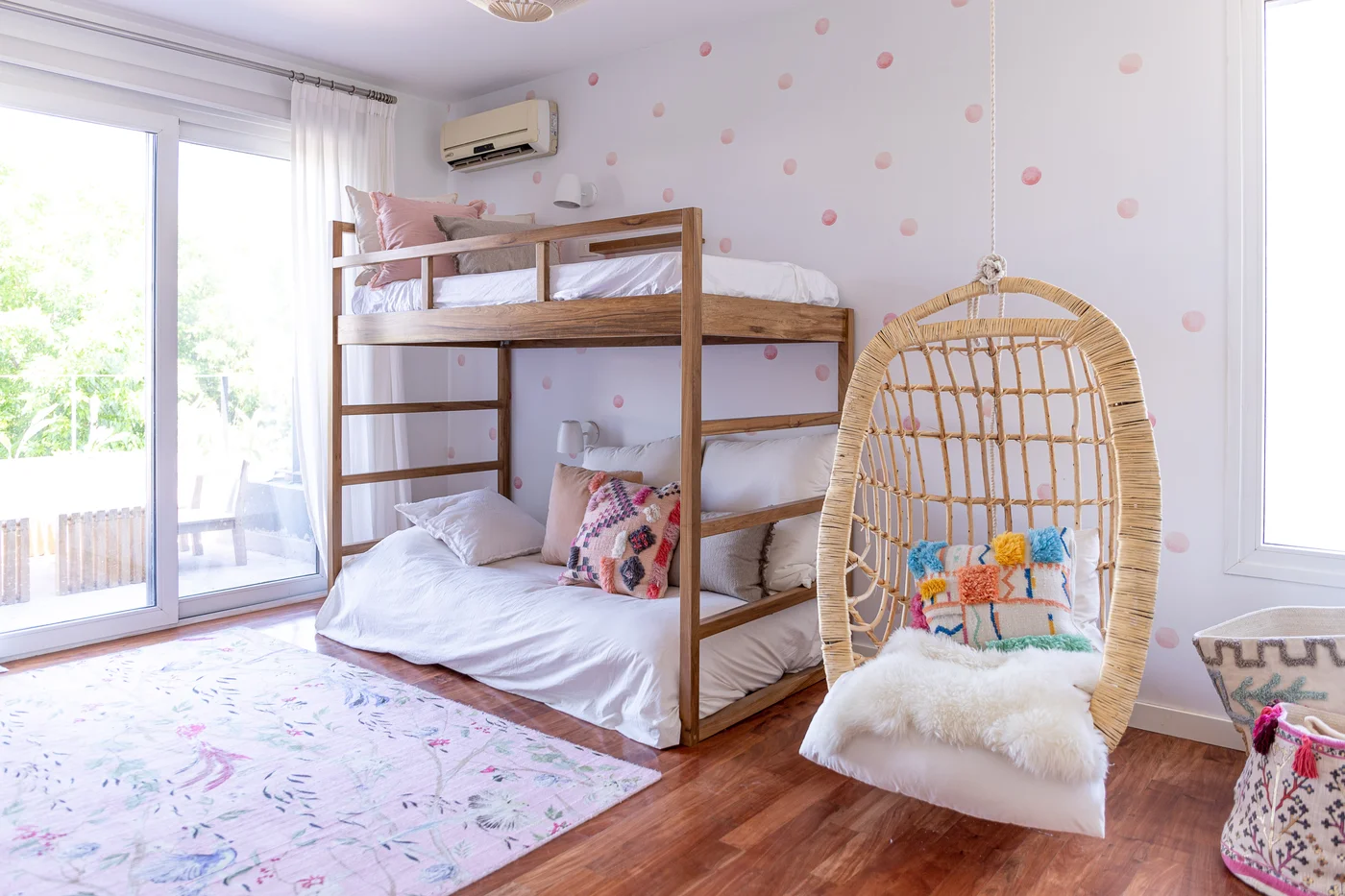 Dormitorio con cucheta de madera, silla colgante y alfombra colorida.