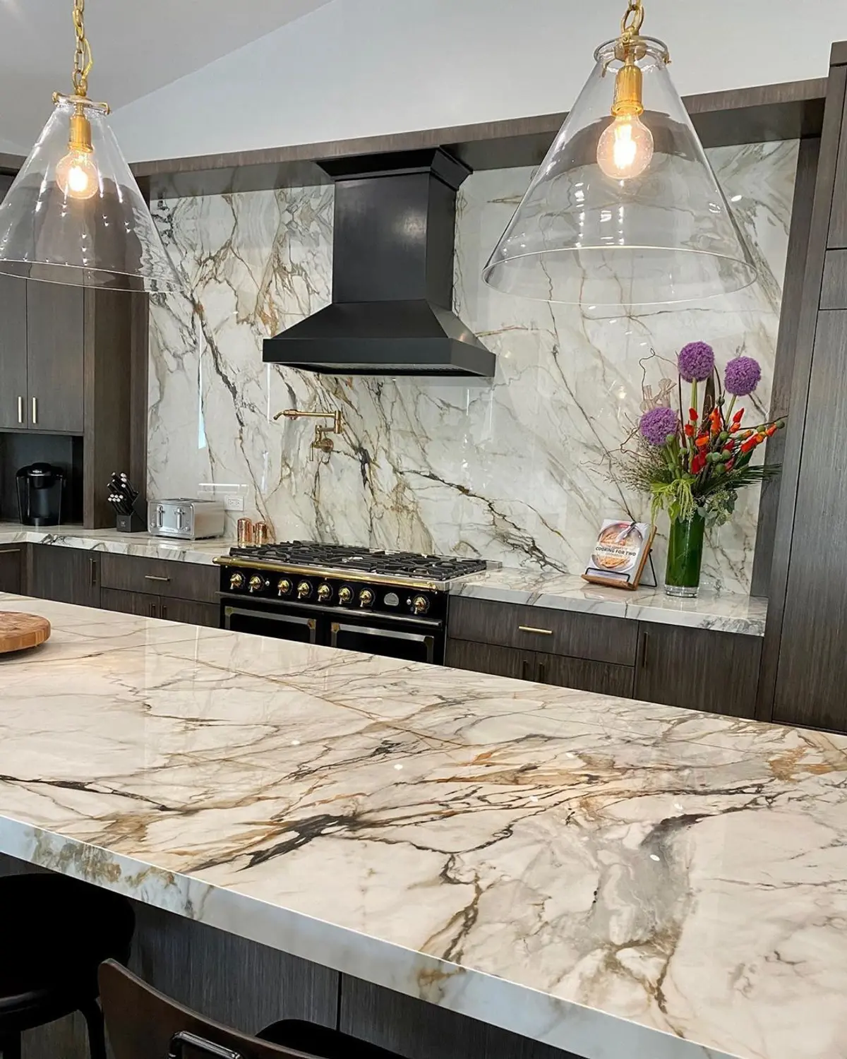 Cozinha moderna com ilha de mármore, coifa industrial e pendentes — projeto COCINAS, por DE STEFANO