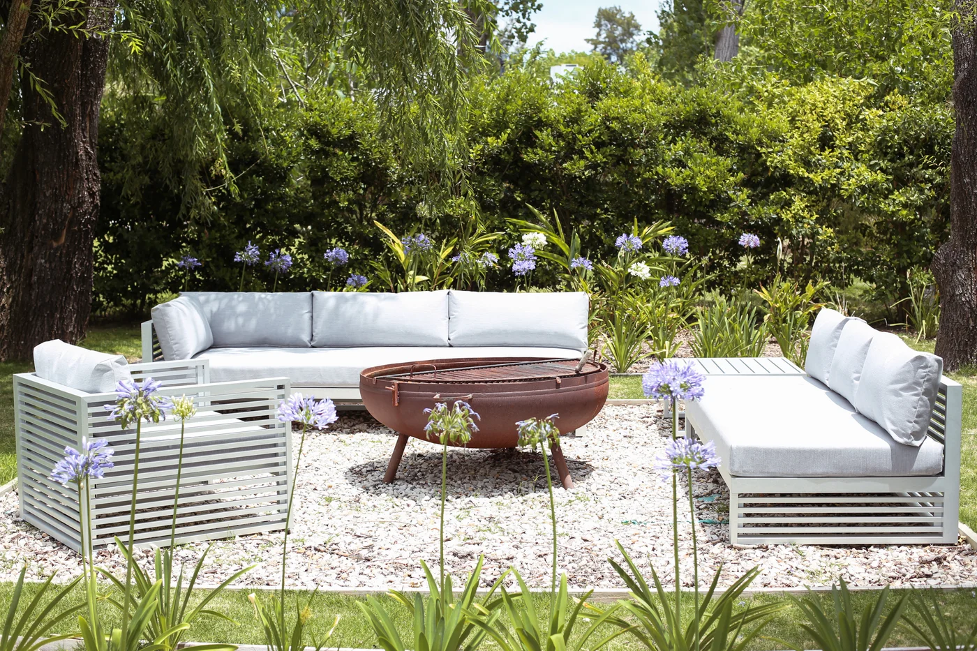 Living exterior moderno con sofás blancos y brasero en jardín