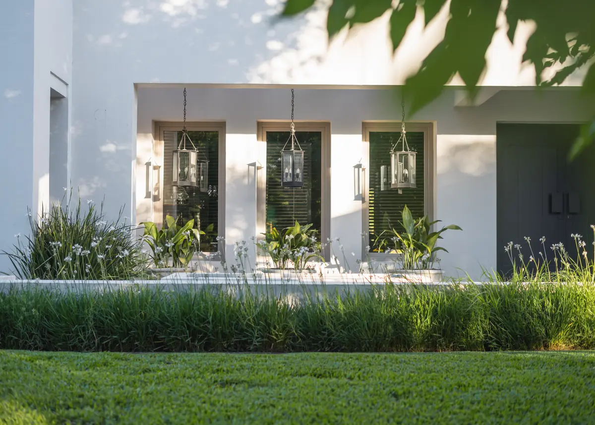 Fachada moderna con iluminación de linternas y vegetación exuberante — proyecto Pilará ll - Interiorismo , por Estudio Etiqueta, en Pilará