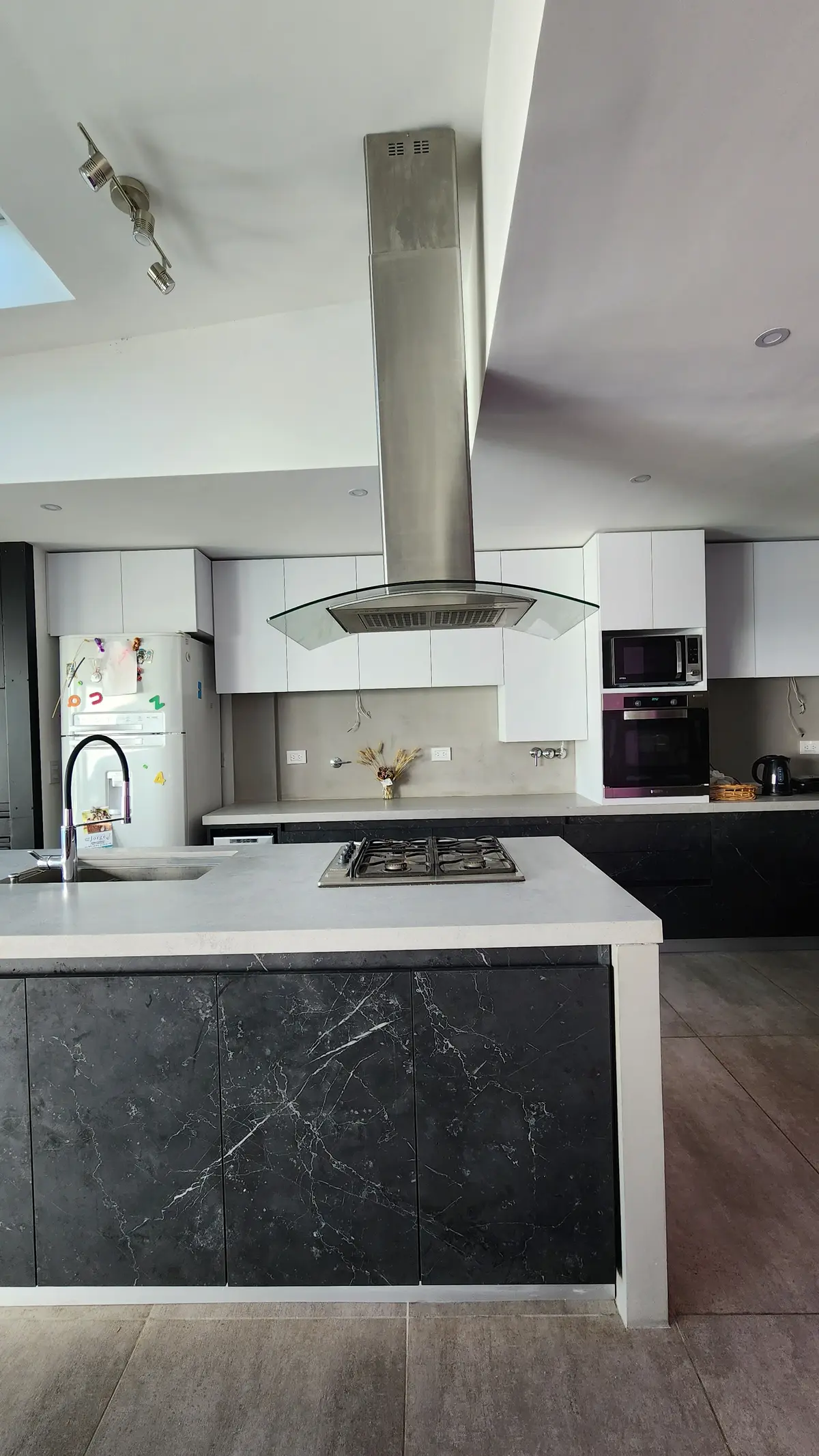 Cocina moderna con isla de mármol oscuro y campana extractora central — proyecto Casa Berner, por Zima Arquitectura, en La Plata