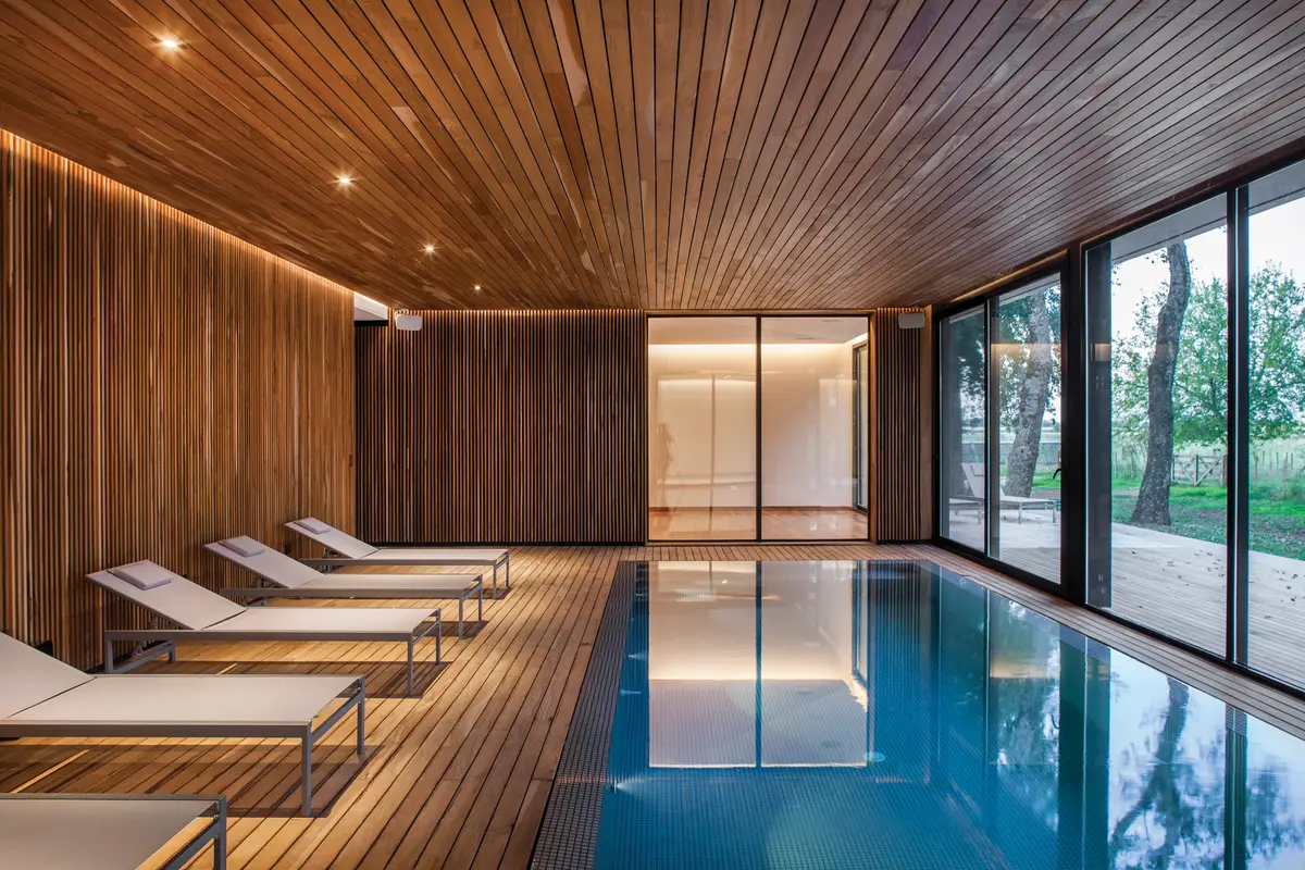 Área de piscina interna moderna com revestimento de madeira — projeto Spa La Fantasía, por Mazzinghi Sanchez