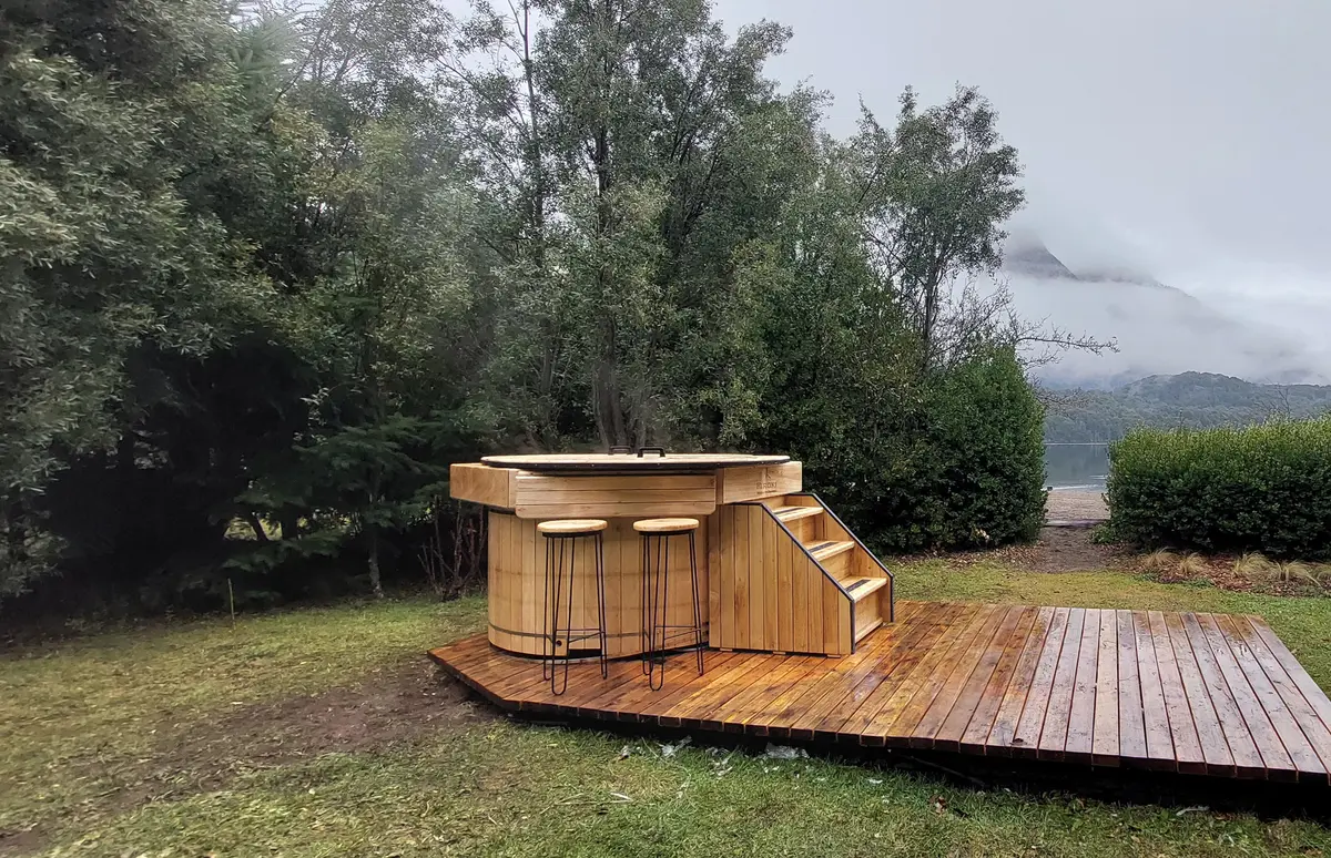 Jacuzzi externo de madeira com deck e bancos altos em ambiente natural — projeto Cabañas Pruden - Bariloche, por ARM ARQUITECTOS, em San Carlos de Bariloche