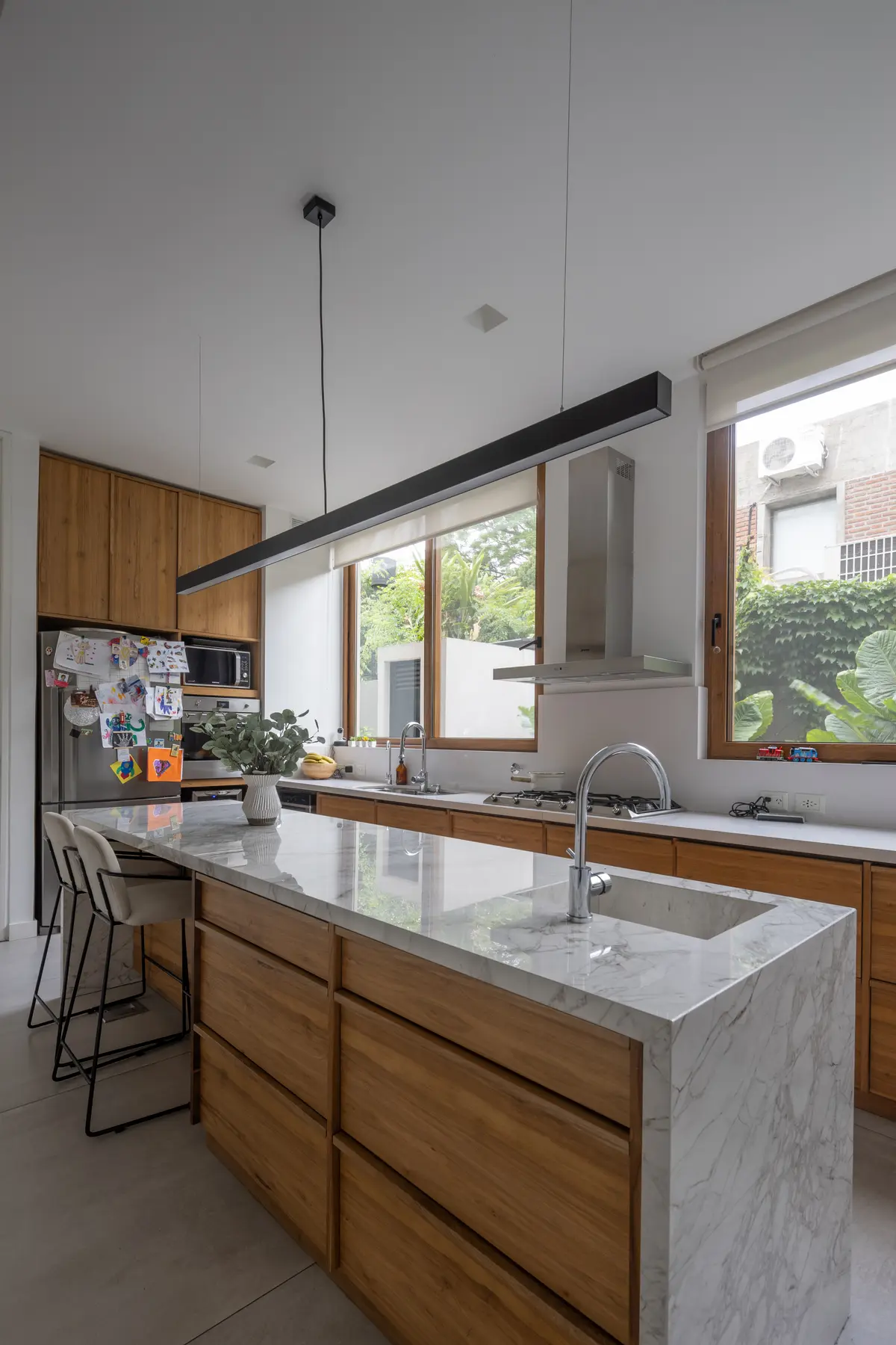 Cocina moderna con isla central, madera natural, mármol y ventanales — proyecto CASA OrAz, por Alfredo Orfila arquitectura, en San Isidro