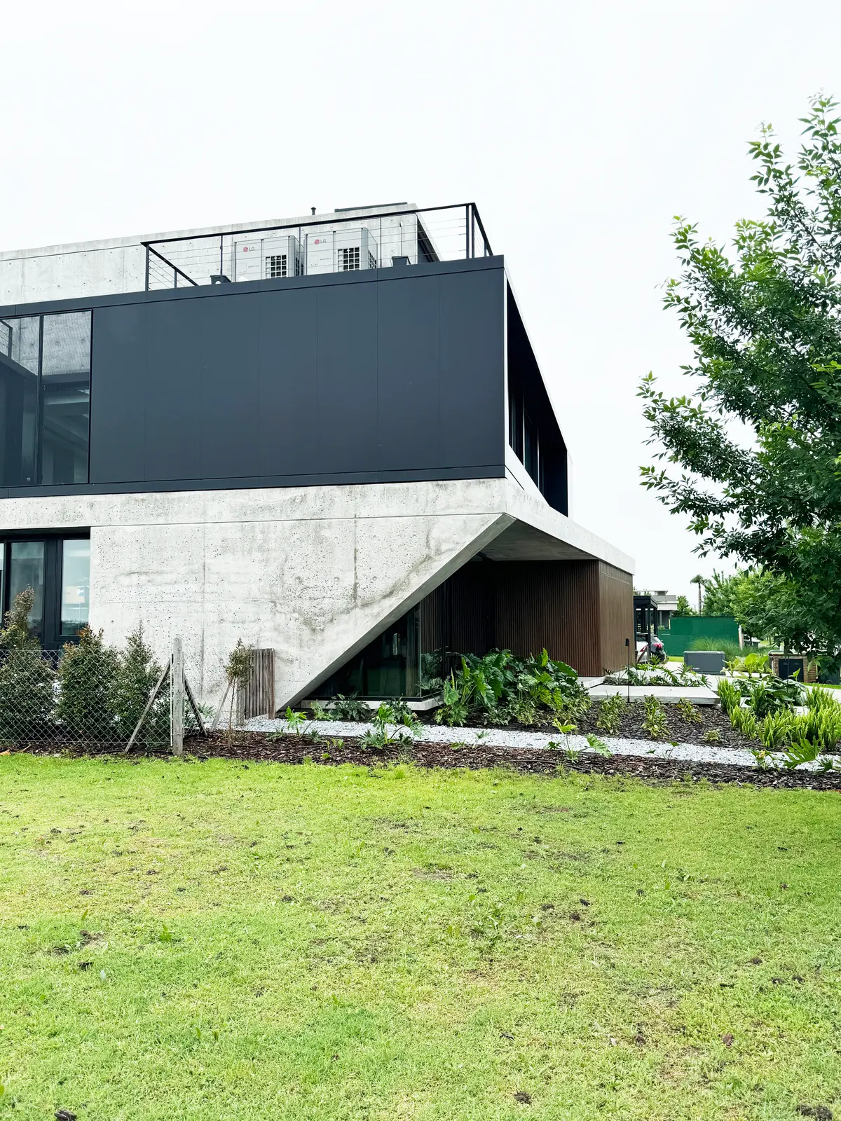 Fachada moderna de concreto com grandes janelas e vegetação integrada — projeto Casa ENE, por Jorgelina Tortorici & asoc., em Nordelta