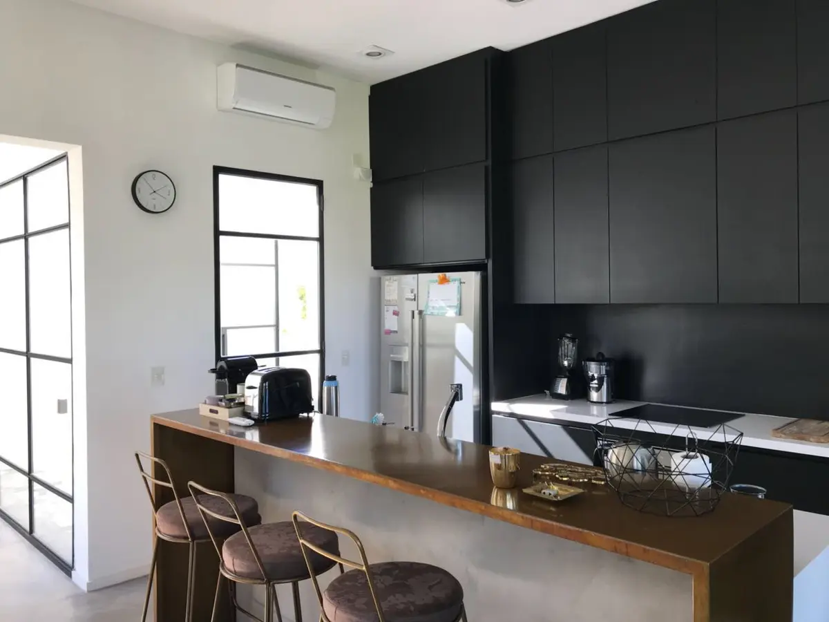 Cocina moderna minimalista con isla de madera y muebles negros — proyecto Casa Las Liebres, por Mazzinghi Sanchez, en Garin