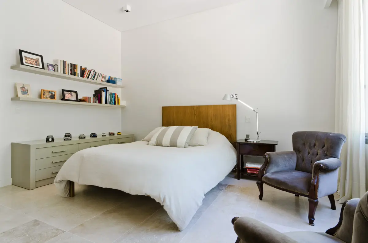 Dormitorio minimalista moderno con cama blanca y sillón gris — proyecto Casa P, por Estudio Dado, en San Isidro