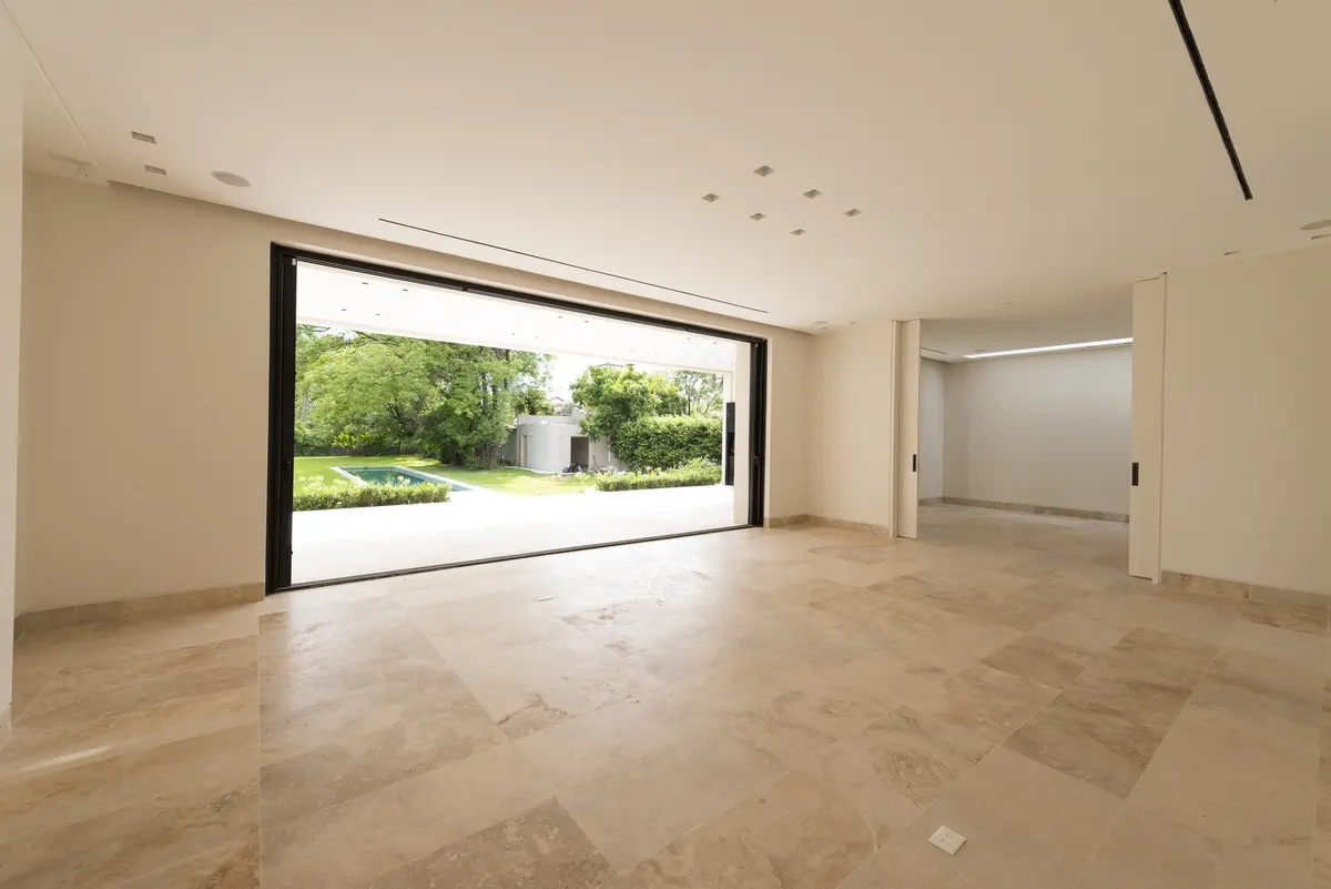 Sala moderna com portas de correr para o jardim e piso de travertino — projeto Casa C, por Estudio Dado, em Belgrano