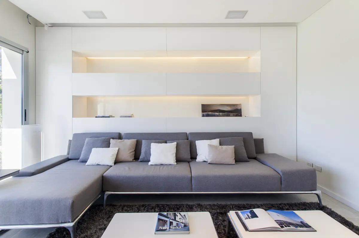 Sala de estar moderna minimalista com sofá modular e prateleiras embutidas — projeto Modernismo Náutico, por Apaarquitectura, em Tigre