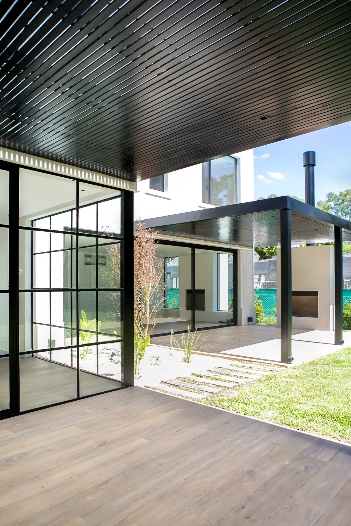 Patio moderno con pérgola de metal negro y ventanales de piso a techo — proyecto Bosque Chico, por Estudio Arq. María Sioli, en Garin
