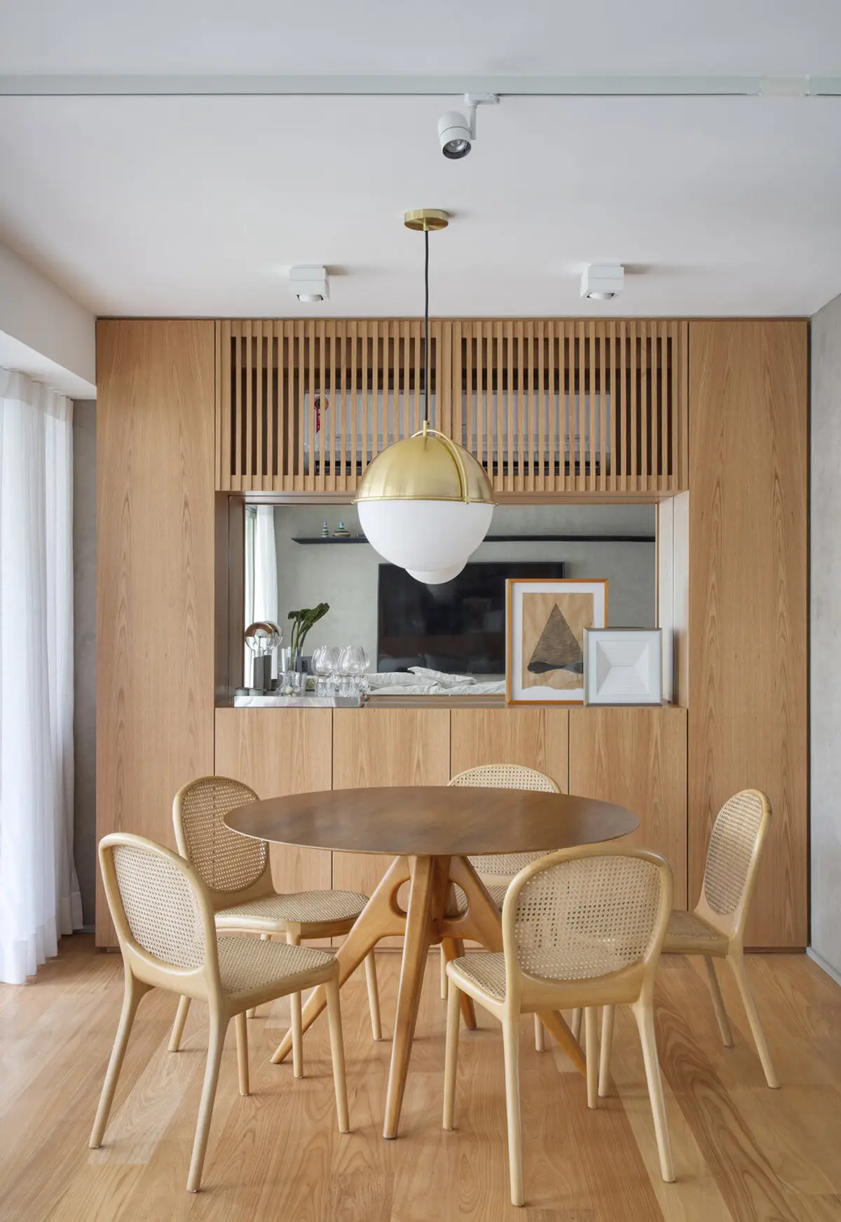 Comedor moderno con mesa redonda y sillas de ratán bajo lámpara dorada — proyecto JG House, por Studio Ro-ca