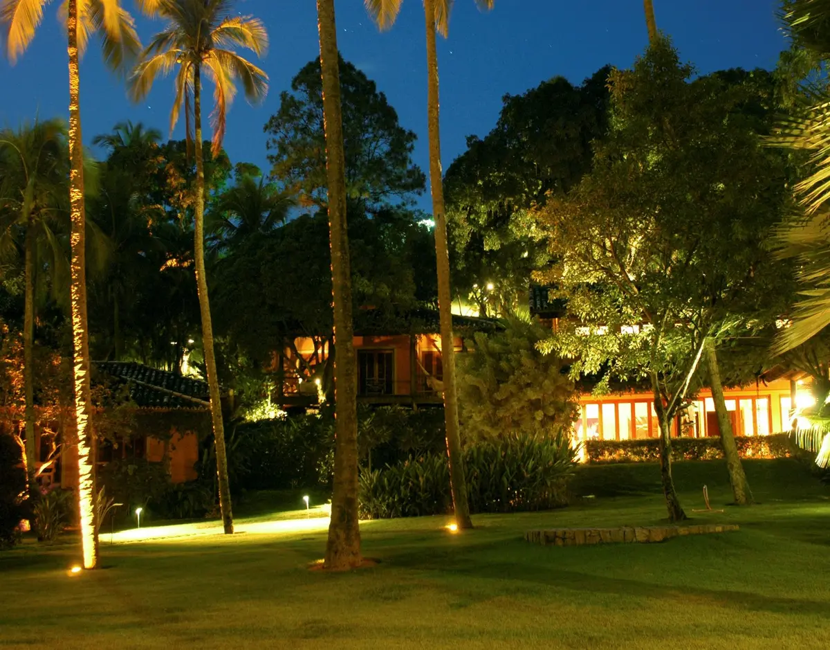 Jardin nocturno iluminado con palmeras y casa de fondo — proyecto Residência RC, por Gil Fialho