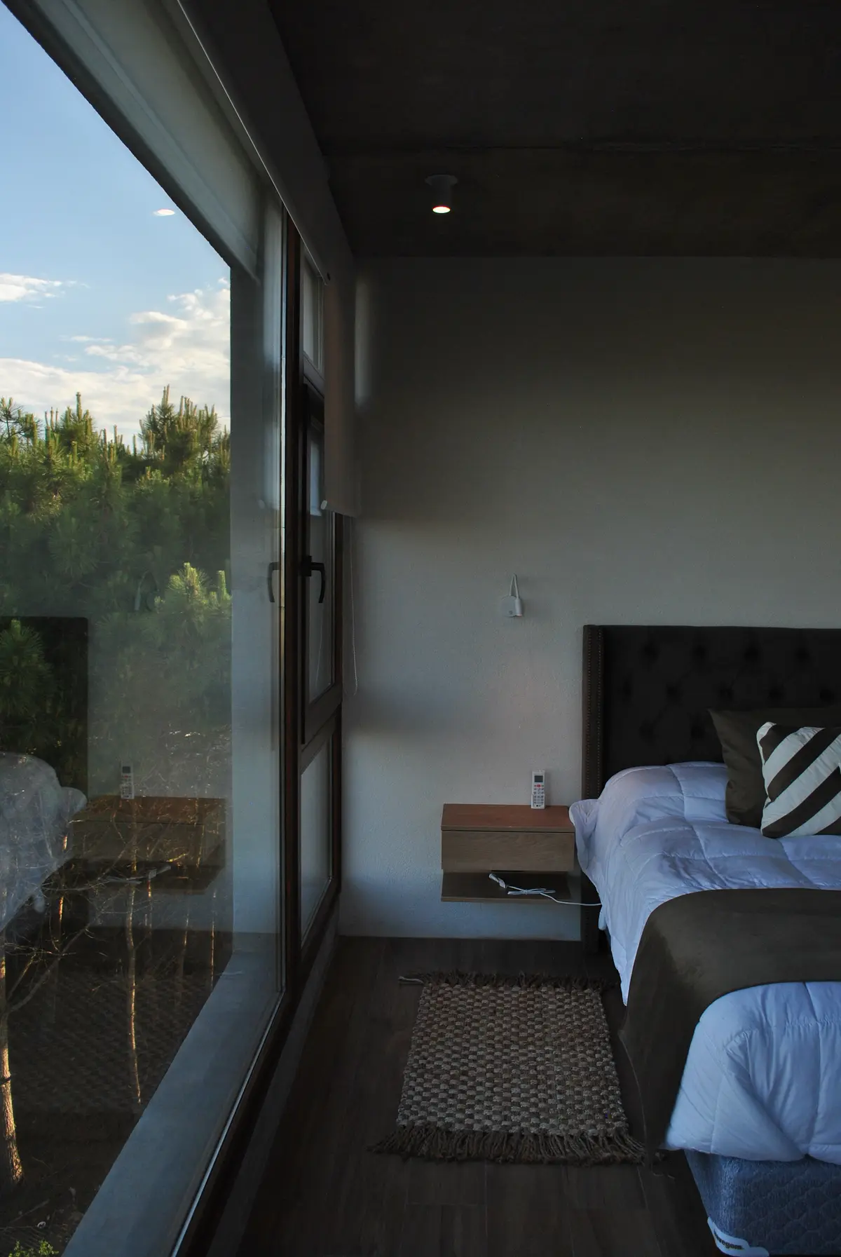 dormitorio moderno con vista al bosque y ventana de piso a techo — proyecto Casa FSC, por TAVA Coop, en Pinamar