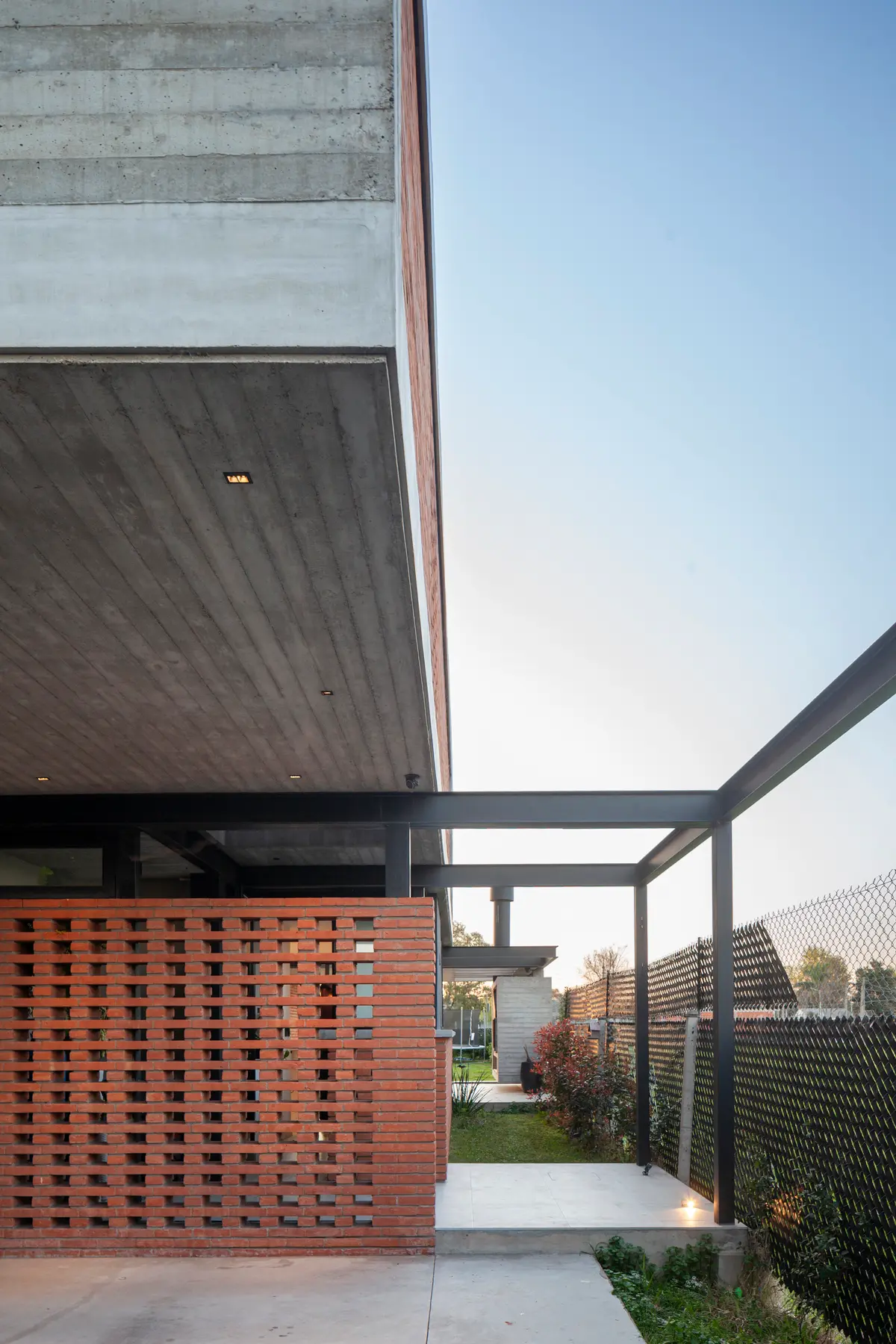 Fachada moderna com tijolo perfurado, concreto aparente e pergolado de metal — projeto CASA BSB, por BUSCETTI & DI BERNARDO arquitectas, em Gonnet