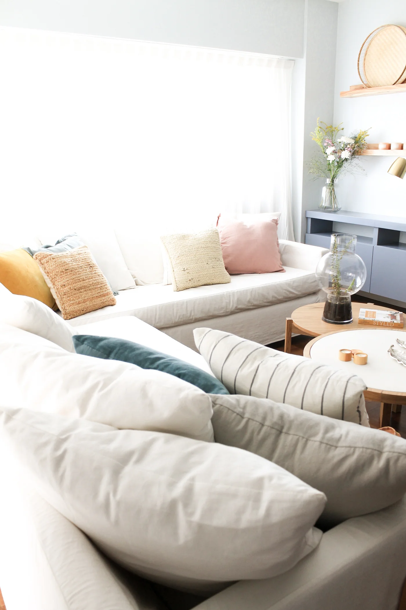 Sofá blanco modular con muchos almohadones y mesa de centro redonda.