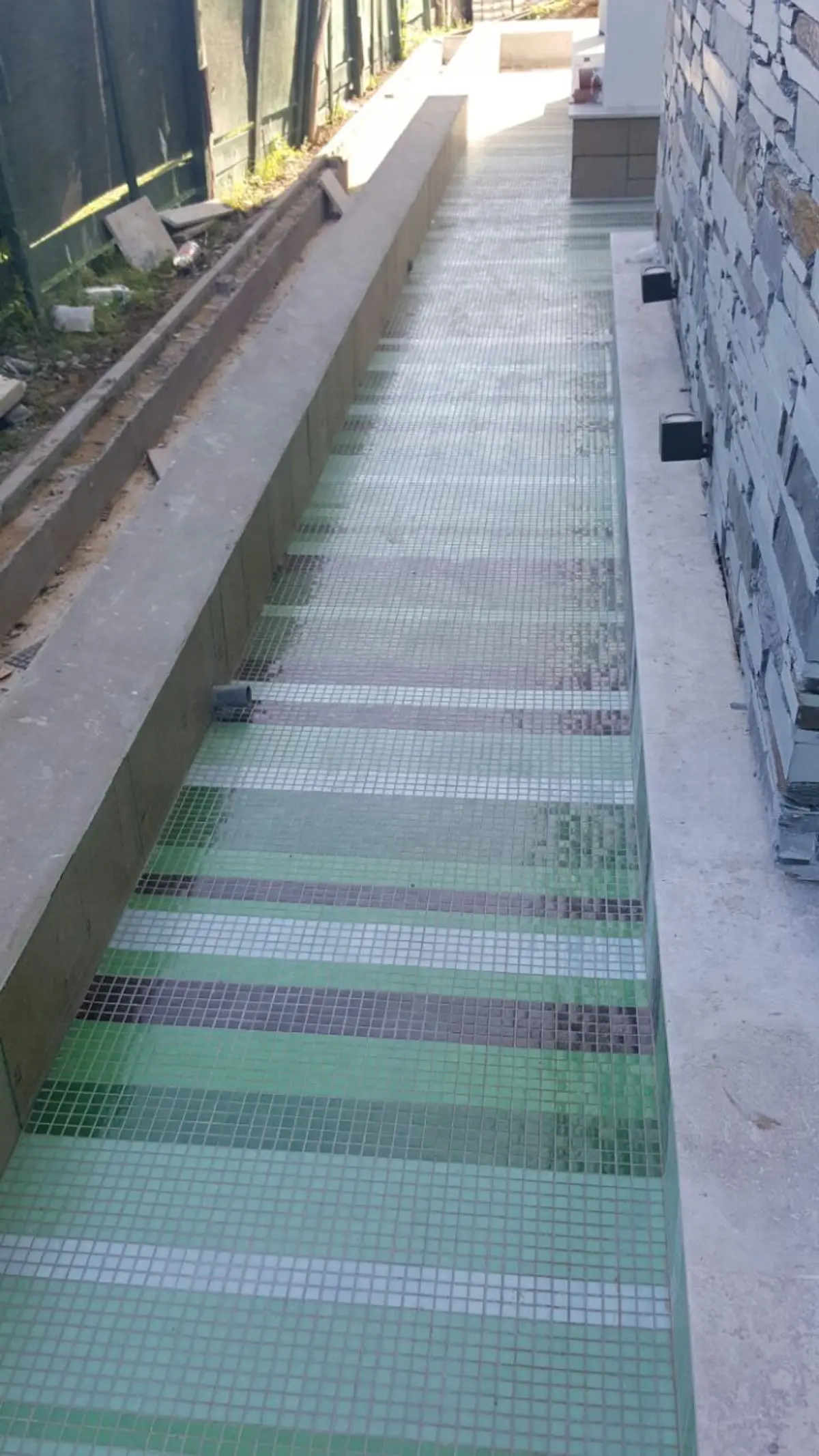 Piscina en construcción con piso de mosaico a rayas y pared de piedra — proyecto CASA GOLF II, por Alejandra Pan Arquitectura, en Nordelta