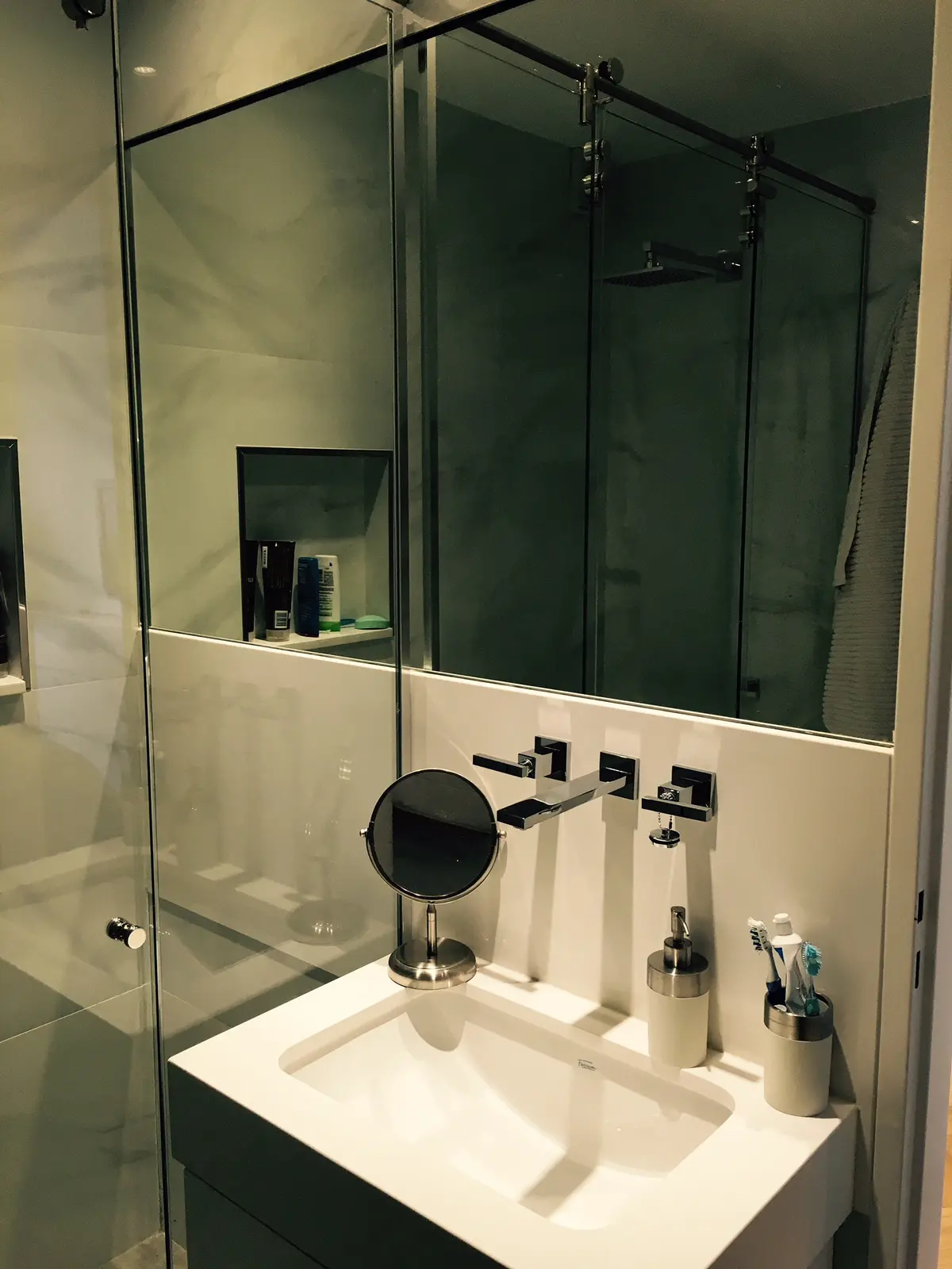 Baño moderno con paredes de microcemento gris, grifería negra y ducha de vidrio — proyecto Ortega y Gasset, por Mgc.arq, en CABA