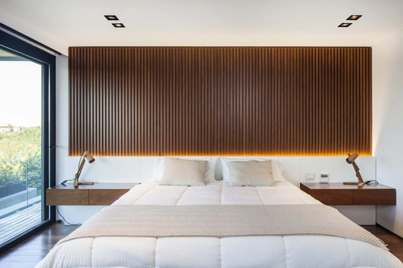 Dormitorio moderno con panel de lamas de madera oscura y luz ambiental.