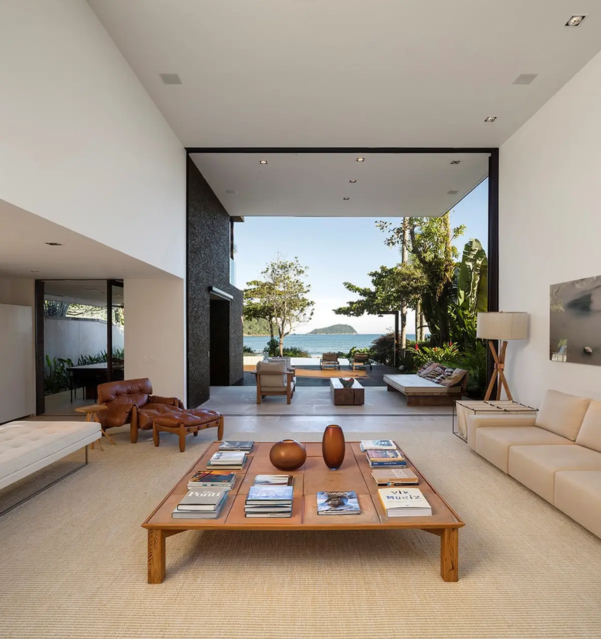 Living minimalista con ventanal hacia bahía, muebles de diseño y vista al mar — proyecto West Whales, por Gil Fialho