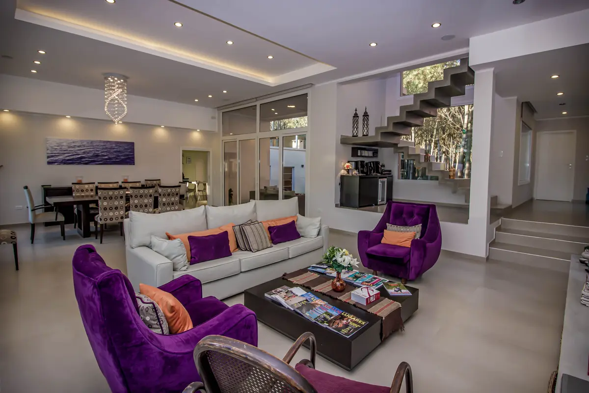 Living moderno con escalera flotante y sillones morados — proyecto Vivienda Unifamiliar en Pinamar, por Estudio Schifano, en Pinamar