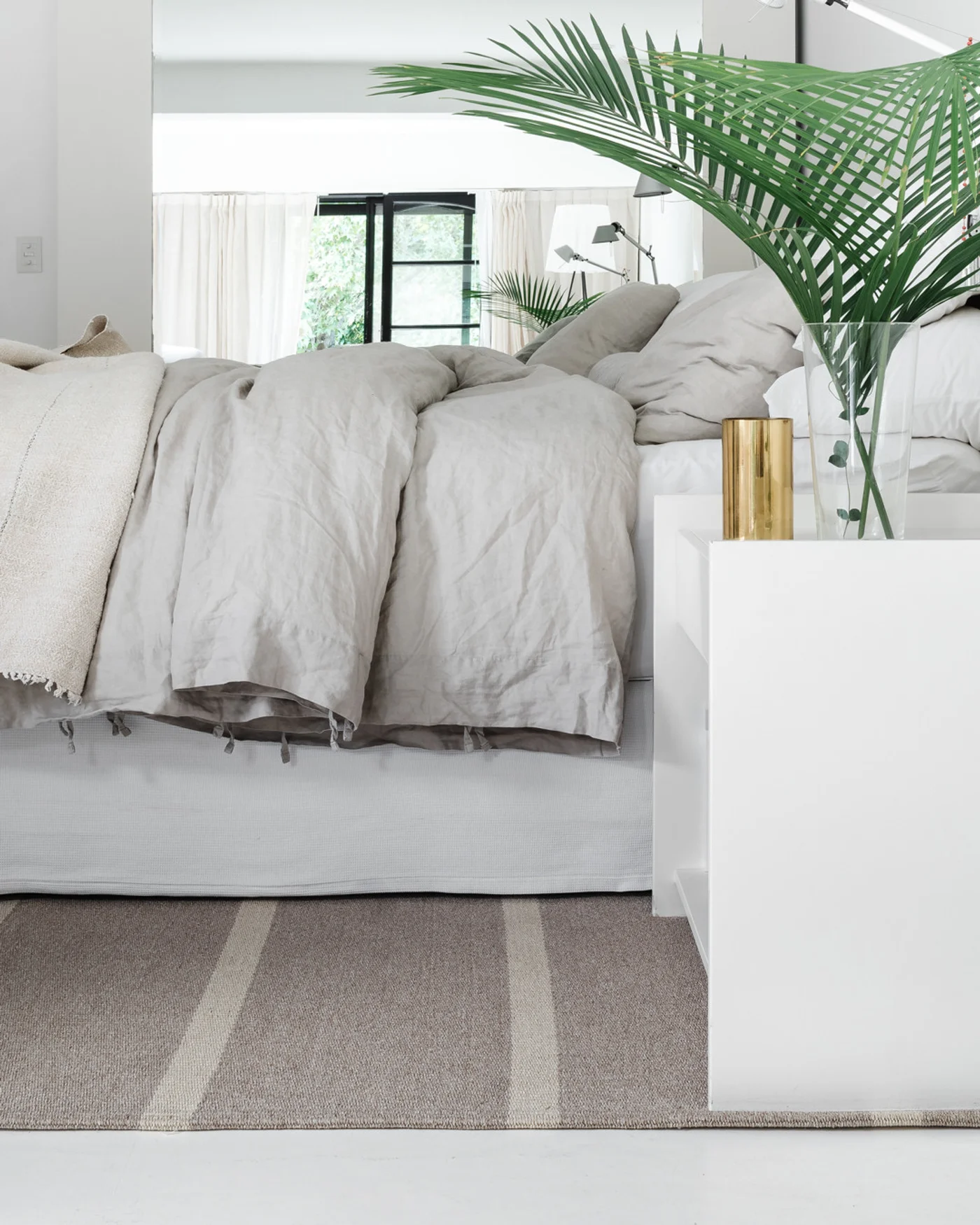 Dormitorio escandinavo minimalista con ropa de cama de lino y planta grande.