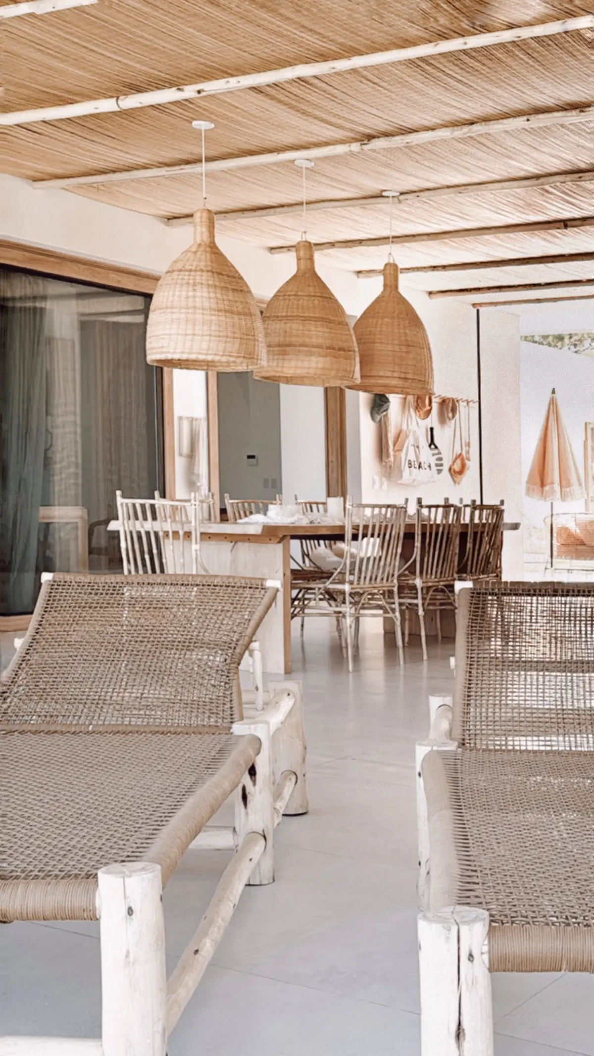 Sala de jantar externa estilo boho-mediterrâneo com móveis de rattan e vigas de madeira — projeto El Refugio, por Grupo Pauta Arquitectura, em Pinamar
