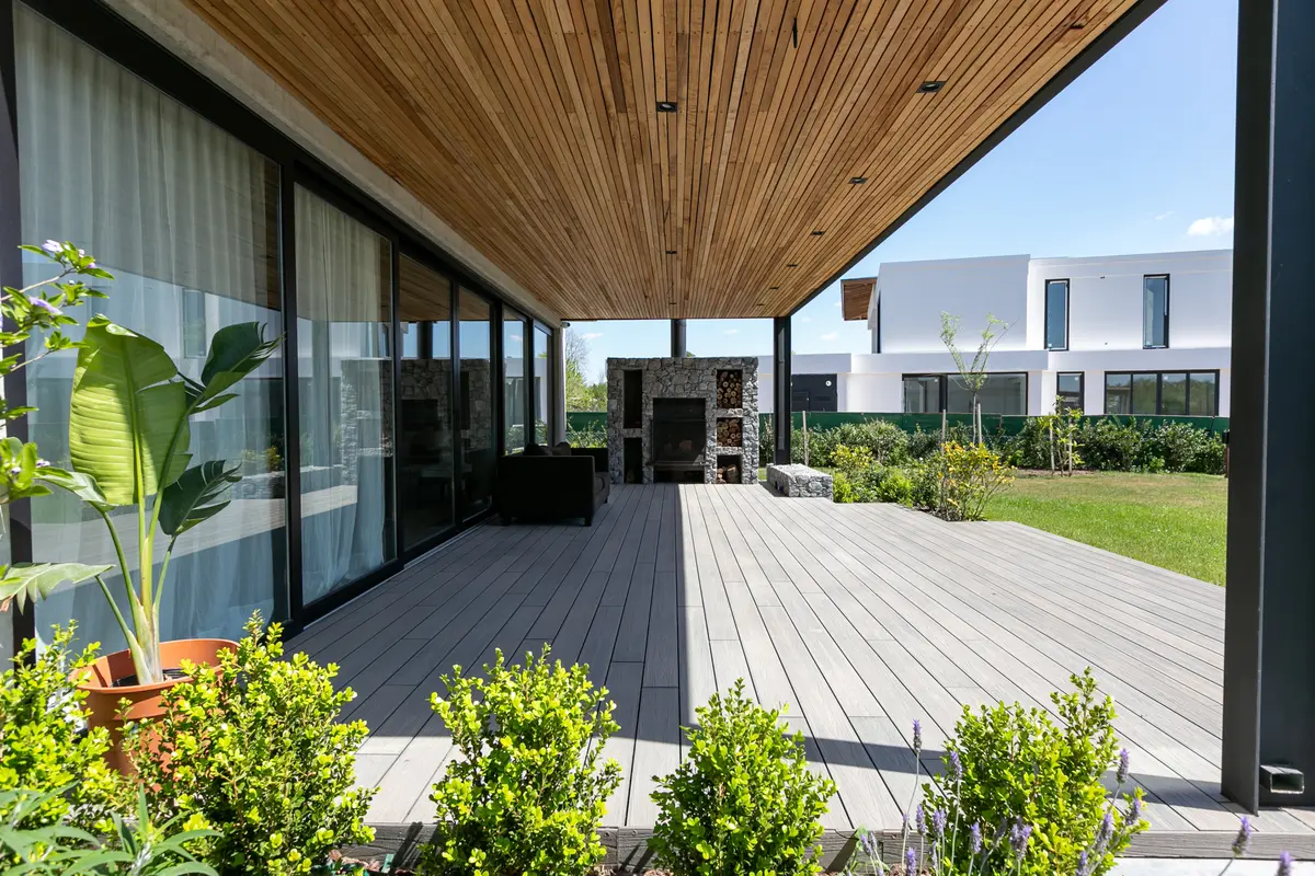 Amplio deck de madera gris con techo de listones de madera natural y chimenea exterior — proyecto La volanta 152, por ATO Arquitectos