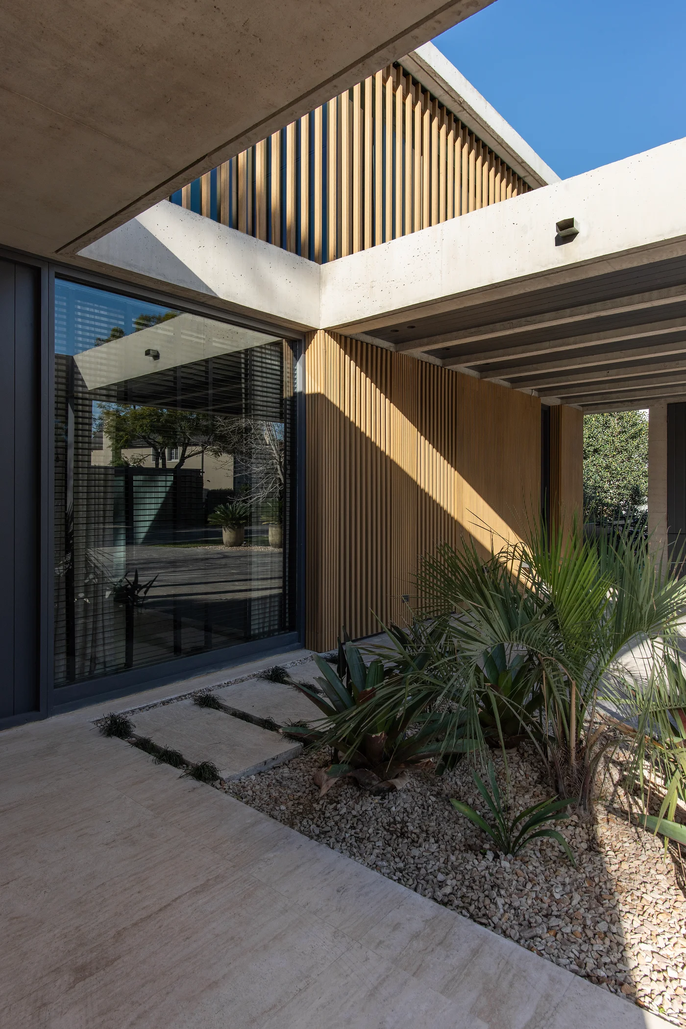 Fachada moderna con revestimiento de madera y concreto, plantas tropicales.