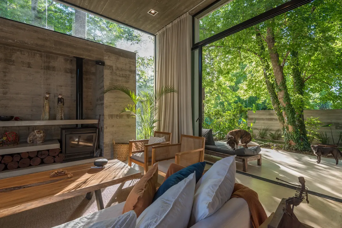 Living moderno de hormigón y madera con grandes ventanales al bosque — proyecto CASA LAS TRANQUERAS, por IMF INÉS MARTINEZ FERRARIO