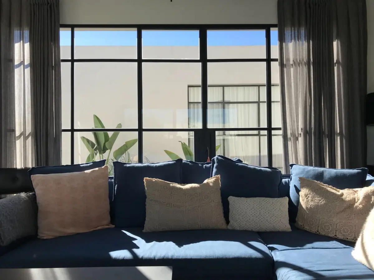 Sala moderna com sofá azul profundo e grande janela em grade — projeto Casa Las Liebres, por Mazzinghi Sanchez, em Garin