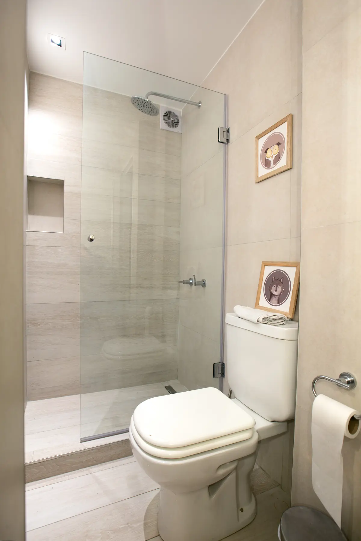 Baño moderno con ducha acristalada, azulejos beige y cuadros con rostros — proyecto Callao, por Mgc.arq, en CABA