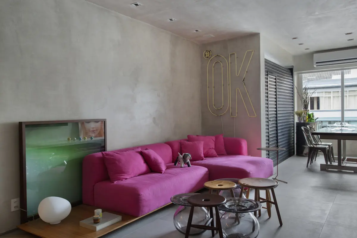 Living moderno con sofá fucsia, piso hormigón y neon OK en pared — proyecto MM House, por Studio Ro-ca