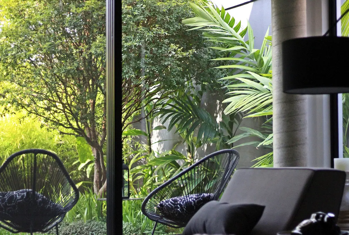 Terraza con sillas de mimbre negro y vista al jardín arbolado — proyecto Residência VT, por Gil Fialho