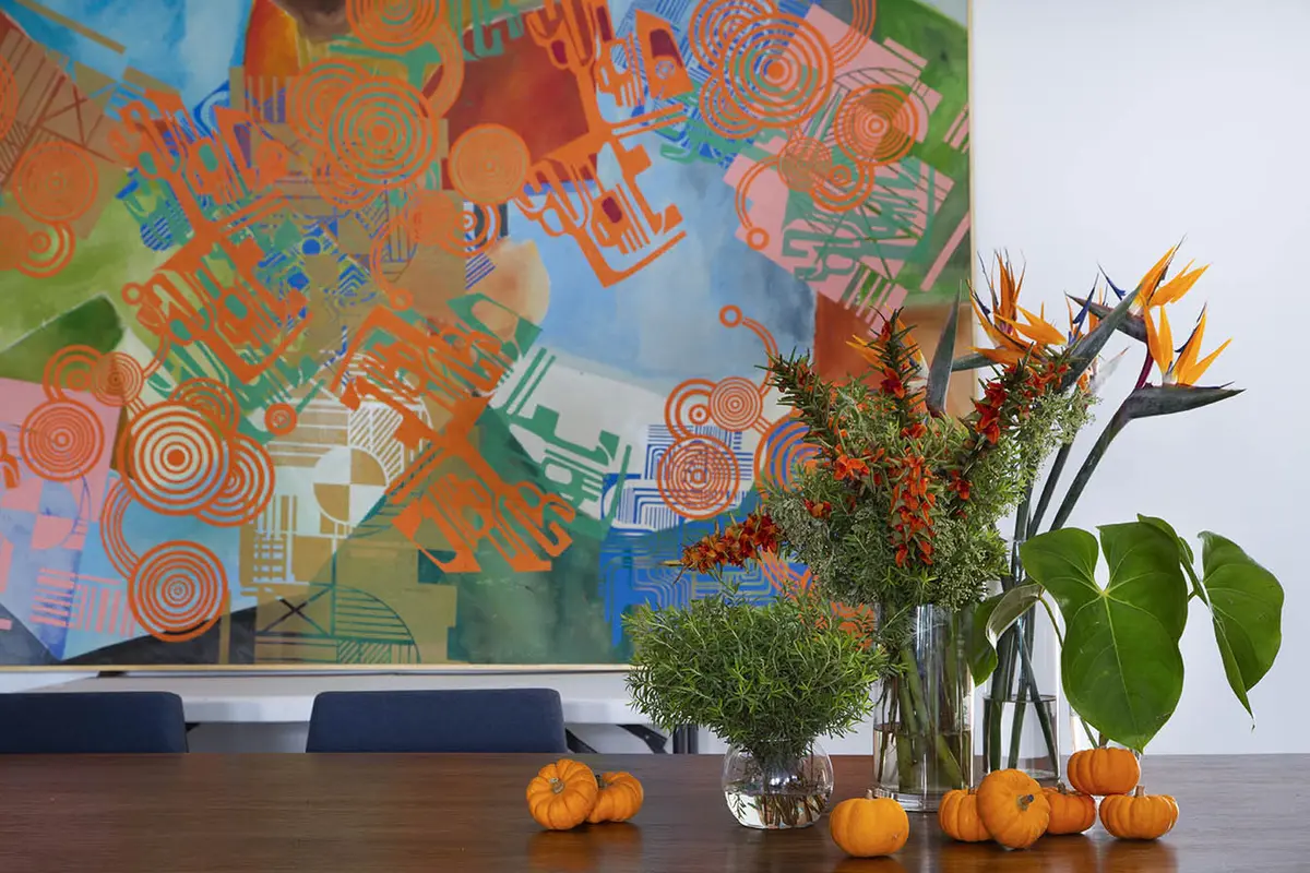 Oficina moderna con arte abstracto, flores y decoración otoñal sobre escritorio — proyecto Casa Jardim Guanabara, por Amanda Miranda