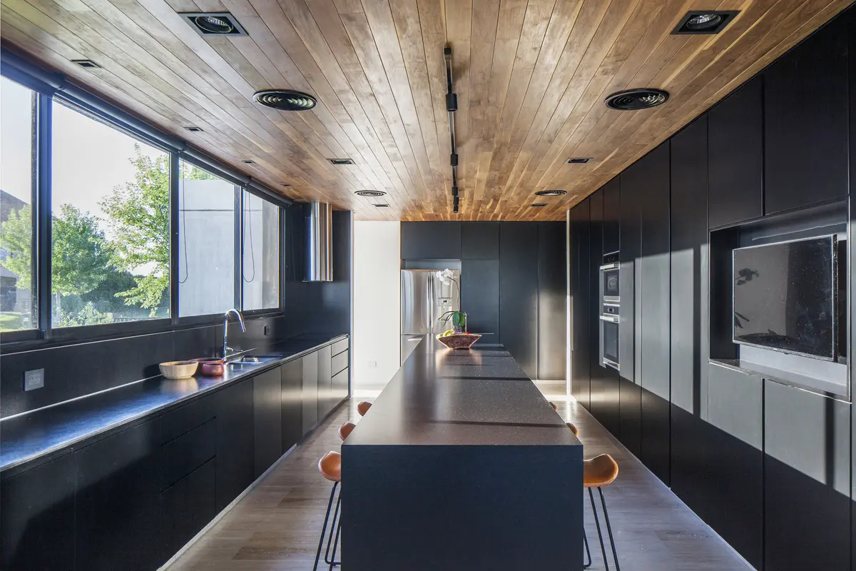 Cozinha moderna longa com ilha central e teto de madeira — projeto Casa Sakura, por Estudio PK