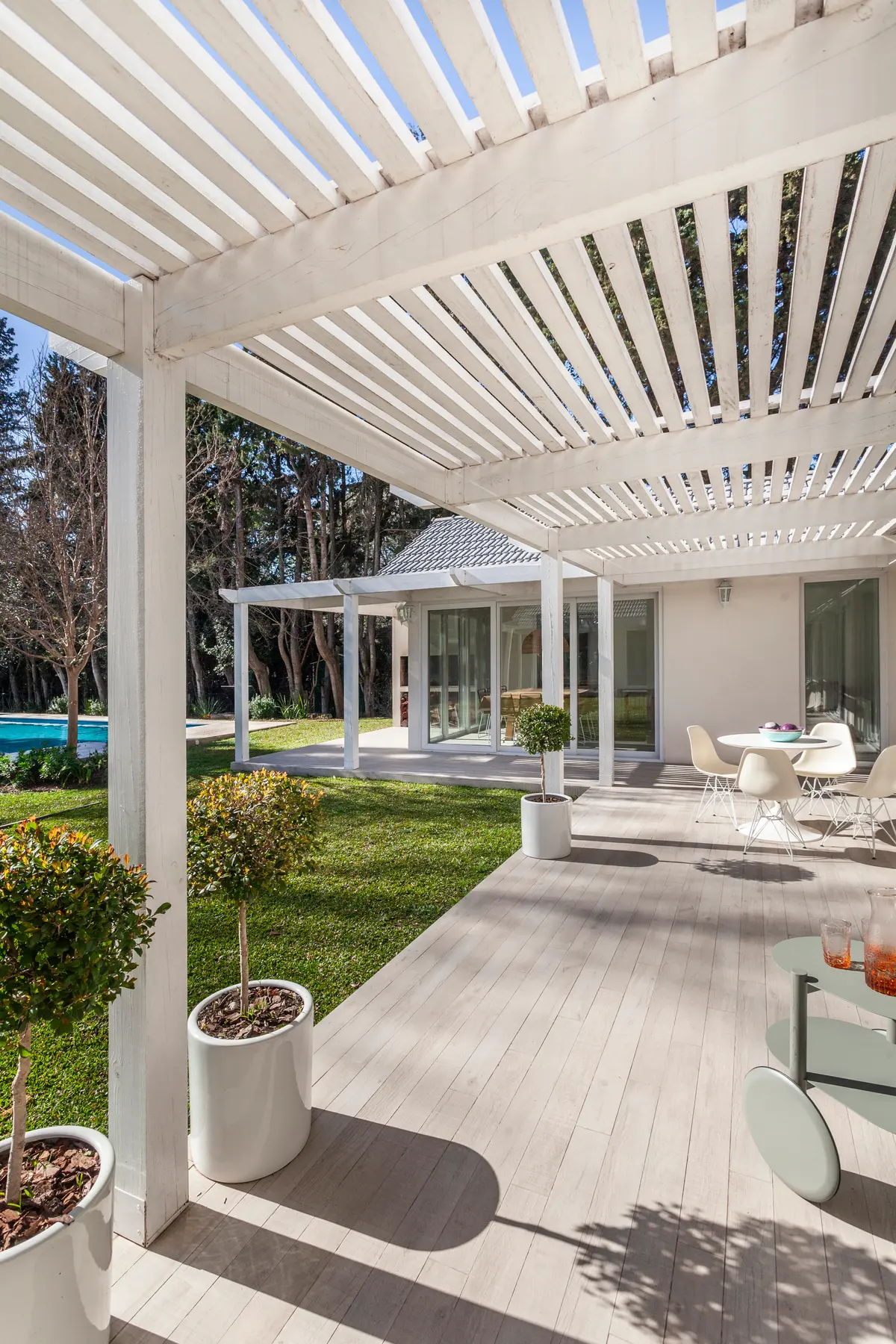 Pátio moderno com pergolado branco e vegetação — projeto Highland, por Lala Loviscek arquitecta, em Pilar