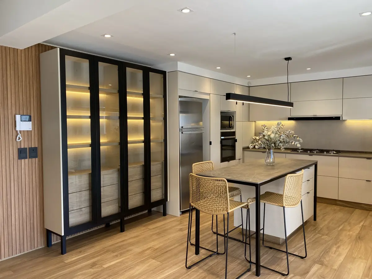 Cozinha moderna com ilha, armário vitrine alto e iluminação quente — projeto Casa en Martinez, por JT ARQUITECTURA, em Martínez