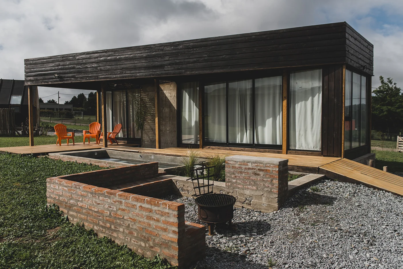 Casa moderna negra con deck de madera y jardín, fachada vidriada.